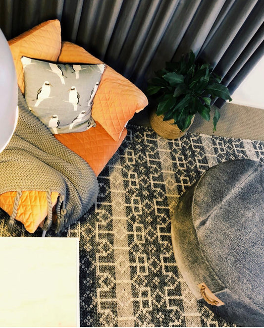 a cowhide ottoman on a area rug with peach arm chair, blanket and scatter cushion