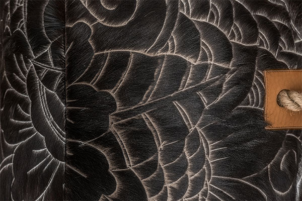 close up of cowhide ottoman with intricate, etched floral and swirl pattern in black and cream