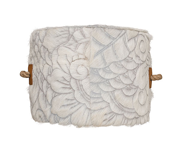 cowhide ottoman with intricate, etched floral and swirl pattern in gray and cream. Tan leather side tabs with thick, jute handles.