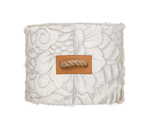 cowhide ottoman with intricate, etched floral and swirl pattern in gray and cream. Tan leather side tabs with thick, jute handles.